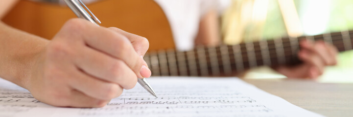 Close-up of female composer writing music notes in notebook.