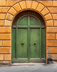 Naklejka premium Green wooden door with two doorknobs set inside terra cotta tilework in the medieval city of Siena in the Tuscany region of Italy. 