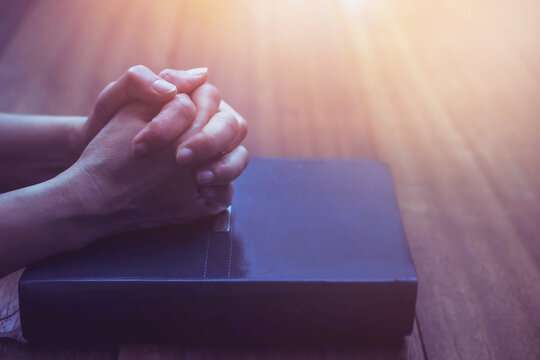 Close up of a woman hands praying on the holy bible on a wooden table with window light Bokeh, Christian praise and worship, devotional concept background with copy space.