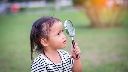 Asian little girl is using magnifying glass to play in the park.SSTKHome