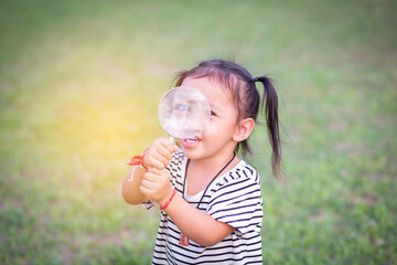 Asian little girl is using magnifying glass to play in the park.SSTKHome