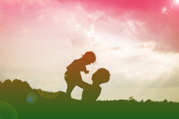 A silhouette of a happy young mother harmonious family outdoors. laughing and playing in the summer...