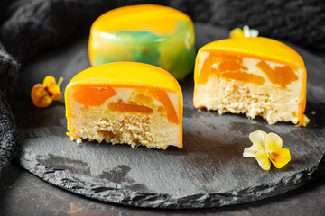 Gourmet Entremet with layered sponge cake, mango jelly and mousse, covered in a mirror tropical coloured mirror glaze.