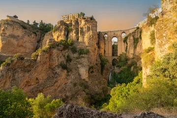 Papier Peint photo Ronda Pont Neuf Daytime landscape photo of the Puente Nuevo bridge in Ronda, Andalusia, Spain. The bridge and surrounding cliffs are bathed in golden light.