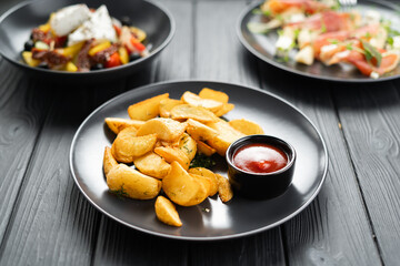 A plate with fried potatoes and ketchup on a dark table in a restaurant. Fast food food concept