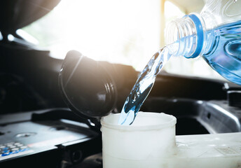 Close up of a bottle of water being poured into a windshield washer tank.