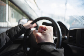 Angry driver is shaking by his fist sitting by the car steering wheel.