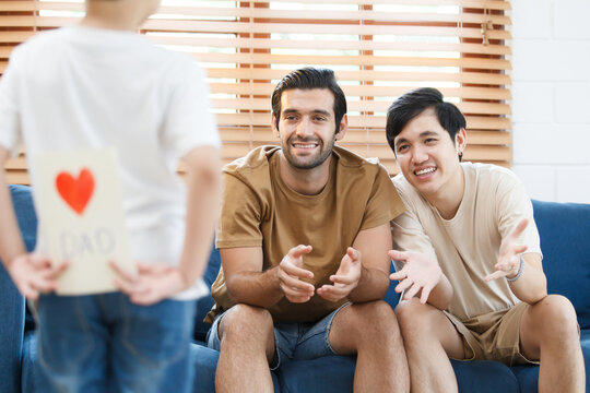 Asian lovely little boy happy to give his dad a Father's Day greeting card and present while living together in living room, diverse gender and lifestyle concept.