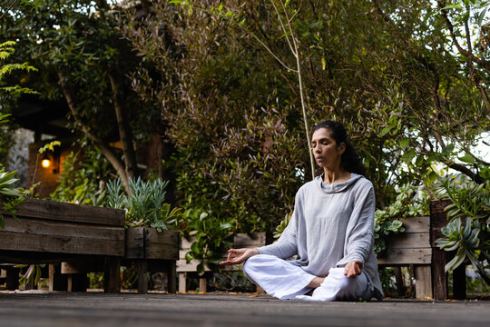 Biracial woman doing yoga, meditating on terrace in garden, copy space