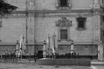 Grayscale shot of chairs, tables, and umbrellas in front of a restaurant in Alcala de Henares, Spain