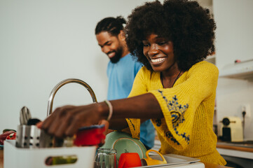 Teamwork at home. An african american couple is doing dishes and cooking dinner at home in the...