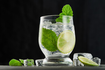 Glass of mojito cocktail with mint leaves and lime pieces and with ice on a dark background. Indoors from low angle view.