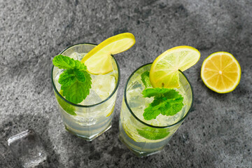 Two tall glasses of mojito cocktail with mint and lime and ice on a dark background. Top view. Studio shot.