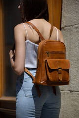 beautiful brunette girl in a blue jeanse and white T-shirt posing with a light brown leather backpack.