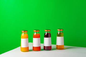 Glass bottles with juice on white table against green background