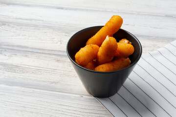 Fried cheese sticks in bowl on wooden table