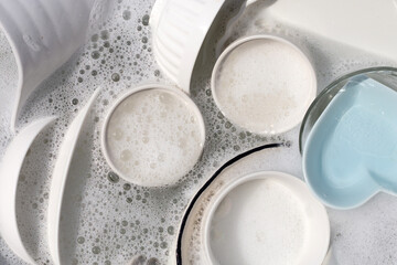 Dishes and bowls in water and bubbles of dishwashing liquid. Kitchen work