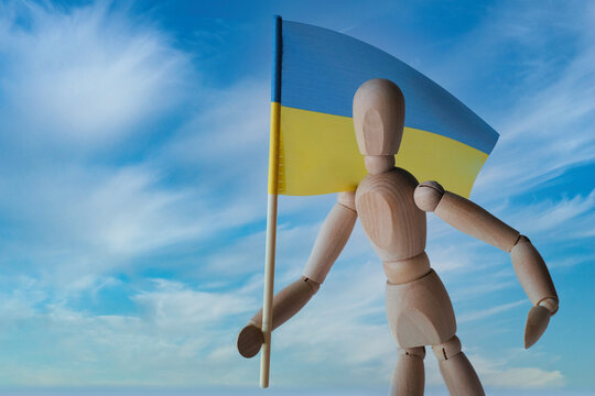 Patriotic wooden mannequin holding the Ukrainian blue and yellow flag against the sky. Stand with Ukraine. Independence Day - 24 of August