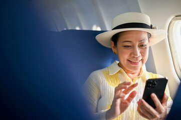 A happy Asian female passenger using her smartphone at her window seat on a flight