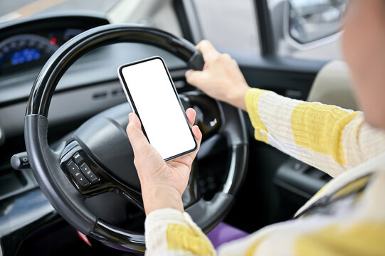 Close-up image of an Asian lady using her smartphone while driving a car.
