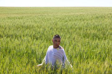 Non binary latin and young gay person has fun among the green wheat field doing different body postures with hands and arms. Concept of diversity, homosexuality and human rights.