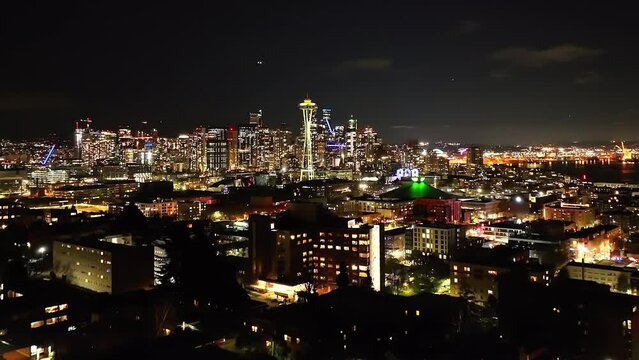City of Seattle skyline at night from a distance, aerial over lit neighborhood in the dark