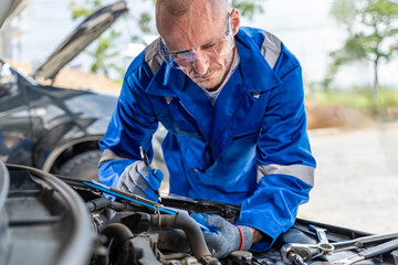 Obraz premium A male car mechanic taking notes for the car repair on his paper notepad while working its engine at his car repair garage