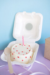 A small bento cake in eco-packaging with a wooden spoon on a purple background without text