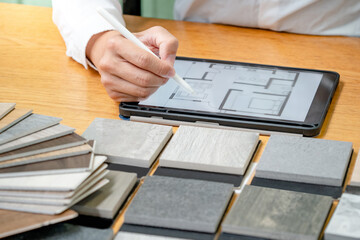 Architect hand choosing stone and wood material samples while drawing on a digital tablet on the...