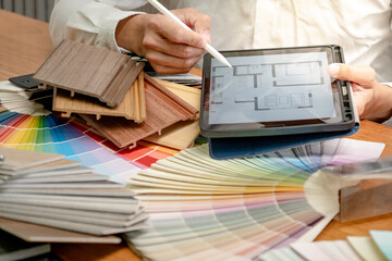 Architect hand drawing on digital tablet choosing sample of color swatch and wood material collection on the table in studio. Designer working for interior architecture and furniture design project