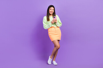 Naklejka premium Portrait of optimistic gorgeous lovely girl wear stylish pullover skirt hold smartphone read post isolated on violet color background
