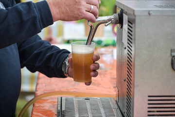 Cold draught beer is poured from a mobile tap in a plastic glass at an open air summer festival, copy space, selected focus - 623365119