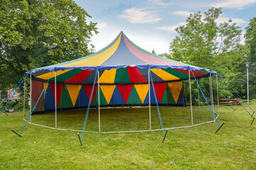 Small colorful circus tent with one pole standing half open on a meadow for a summer party or...