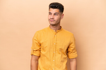 Fototapeta premium Young caucasian man isolated on beige background making doubts gesture looking side