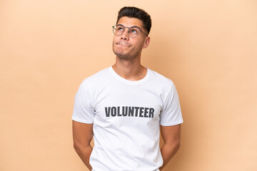Young volunteer caucasian man isolated on beige background and looking up