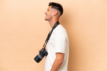 Young photographer caucasian man isolated on beige background in lateral position