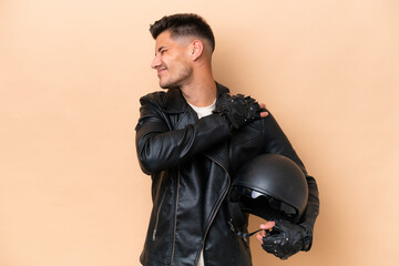 Young caucasian man with a motorcycle helmet isolated on beige background suffering from pain in shoulder for having made an effort