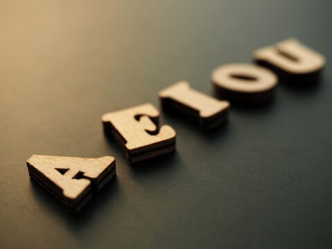 Wooden Uppercase Vowels aeiou on a dark background 