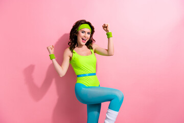 Portrait of overjoyed fitness girl raise fists celebrate success empty space green blue bodysuit isolated on pink color background