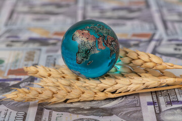 Conceptual story about the global food crisis with ears of wheat, a glass globe and 100 american...
