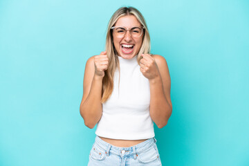 Young caucasian woman isolated on blue background celebrating a victory in winner position