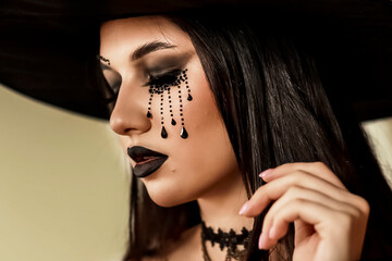 A young girl in the image of a witch, in a black hat and a black dress with makeup in a gothic style looks like a witch, the concept of Halloween ideas