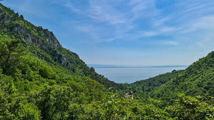 Fototapeta na wymiar A panoramic view on the Mediterranean Sea in Croatia from Vojak. The mountain is overgrown with lush green plants. Few islands in the back. Early morning hiking by the sea. Clear, blue sky. Remedy