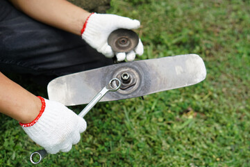 Close up photo of hands wear gloves of a mechanic are repairing and tighten the blade of mowing...