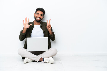 Young Brazilian man with a laptop sitting on the floor isolated on white counting seven with fingers