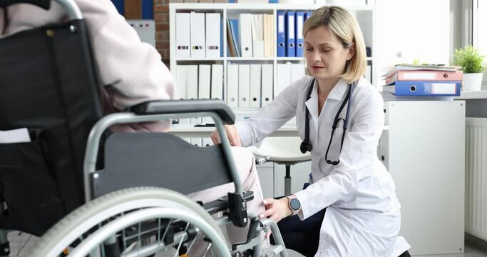 A female doctor hits the knees of a woman in a wheelchair with a hammer. Checking the reflex after injury, disability