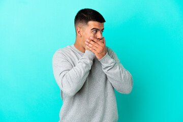 Young handsome man over isolated blue background covering mouth and looking to the side