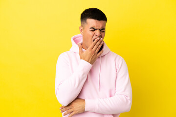 Young handsome man over isolated yellow background yawning and covering wide open mouth with hand