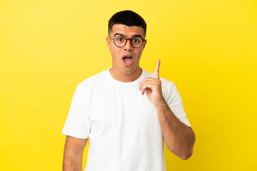 Young handsome man over isolated yellow background intending to realizes the solution while lifting a finger up