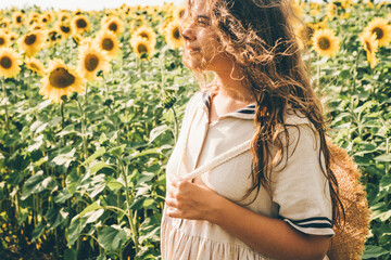 Young woman with curly hair at tha hat in a field of sunflowers. Summer mood.